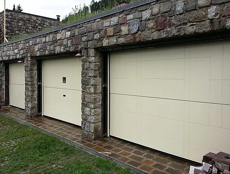 Porte sezionali chiare inserite in un muro in pietra